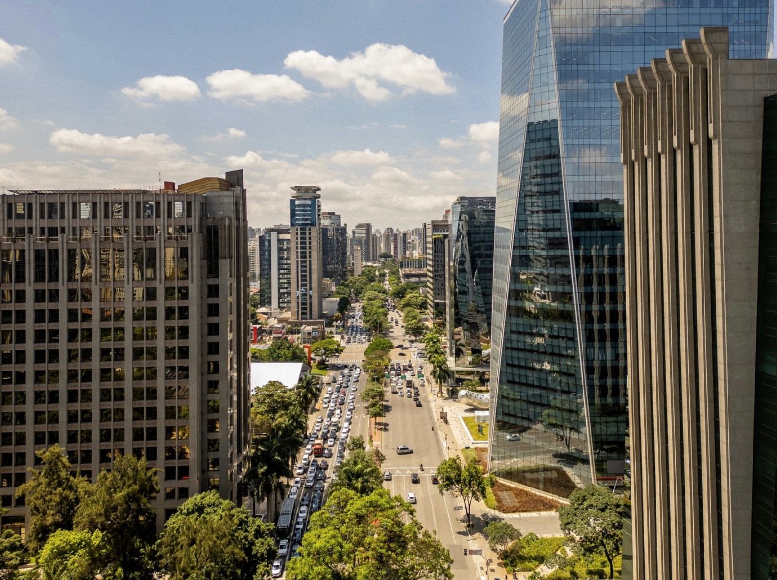 Vista aérea do centro financeiro de São Paulo: avenida arborizada com tráfego intenso entre edifícios corporativos envidraçados